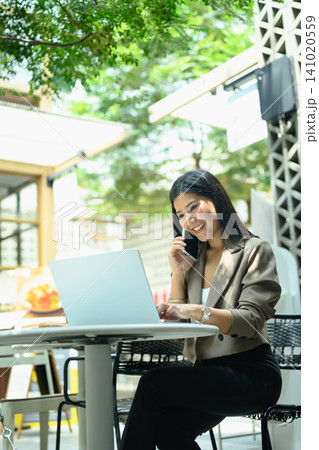 Young business woman working on a laptop and using smartphone sitting on at outdoor cafe workspace Young business woman working on a laptop and using smartphone sitting on at outdoor cafe workspace 141020559