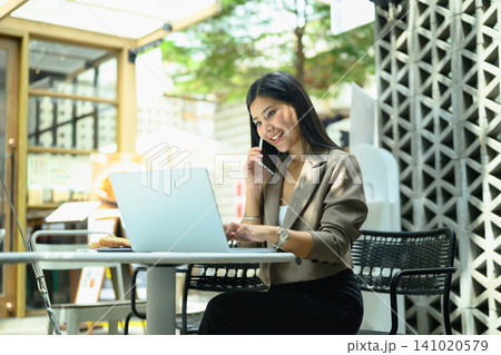 Young business woman working on a laptop and using smartphone sitting on at outdoor cafe workspace Young business woman working on a laptop and using smartphone sitting on at outdoor cafe workspace 141020579