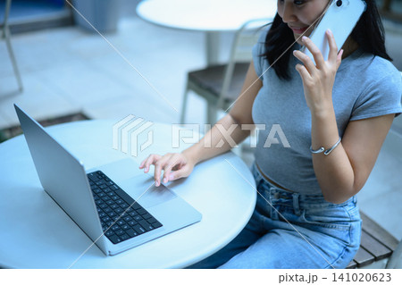 Closeup business woman working on a laptop and using smartphone sitting on at outdoor cafe workspace Closeup business woman working on a laptop and using smartphone sitting on at outdoor cafe workspace 141020623