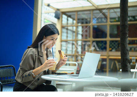 Businesswoman eating toast while working on laptop at cafe Businesswoman eating toast while working on laptop at cafe 141020627
