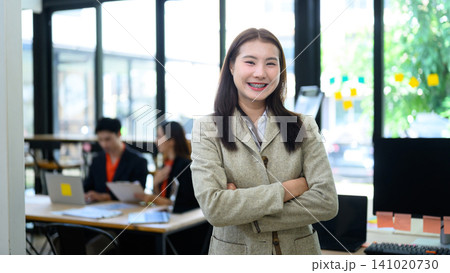 Confident Young Asian Businesswoman Standing with Arms Crossed Smiling in Modern Office Workplace 141020730