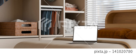 3D Illustrations of Laptop with White Blank Screen Mockup on Bed in Modern Bedroom with Wardrobe 141020780