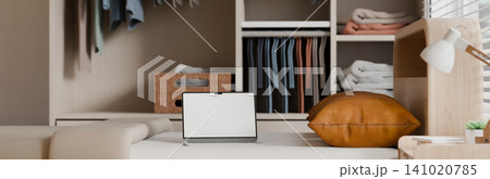 Laptop with Blank White Screen Mockup on Sofa in Cozy Bedroom with Organized Wardrobe Closet Laptop with Blank White Screen Mockup on Sofa in Cozy Bedroom with Organized Wardrobe Closet 141020785