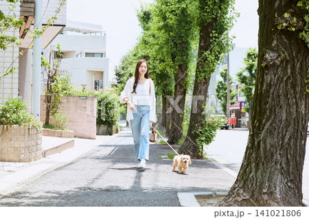 新緑の住宅街で愛犬を散歩する若い女性 新緑の住宅街で愛犬を散歩する若い女性 141021806