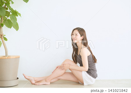 室内で座って脚のスキンケアをする笑顔の若い女性 141021842