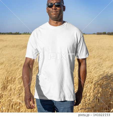 Blank white t-shirt mockup on black man in wheat field at sunset, front view with copy space 141022153