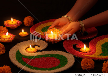 Indian woman holding lit diya lamp over colorful rangoli for Diwali celebration 141023255