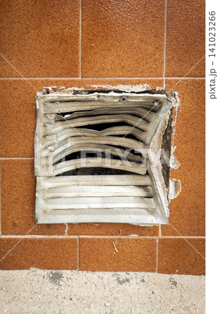 The photo shows a metal ventilation grate that is bent and damaged. It is set into a wall of tiles that are rusty orange. The area looks neglected and needs repair. The photo shows a metal ventilation grate that is bent and damaged. It is set into a wall of tiles that are rusty orange. The area looks neglected and needs repair. 141023266