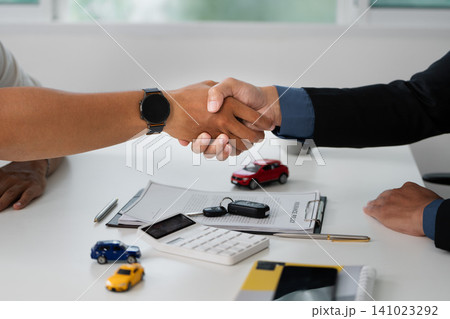 Handshake over desk with toy cars and calculator for car purchase deal Handshake over desk with toy cars and calculator for car purchase deal 141023292