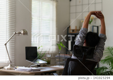 Man stretching arms overhead at desk for workplace wellness and stress relief Man stretching arms overhead at desk for workplace wellness and stress relief 141023294