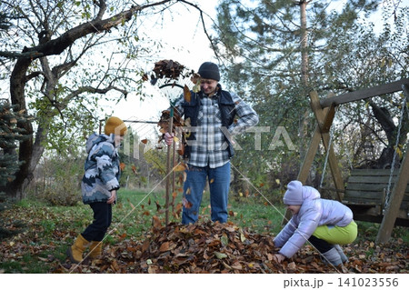 Young father, pre-teen daughter and son in warm autumn clothes spending quality time together among fallen leaves. Happy family enjoying the beauty of fall, playful moments and family life outdoors 141023556