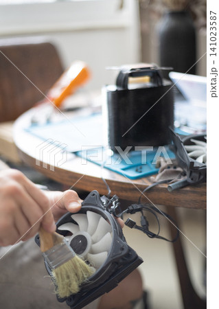 Man cleans a computer fan during a repair session at home in the afternoon with tools and equipment on the table Man cleans a computer fan during a repair session at home in the afternoon with tools and equipment on the table 141023587