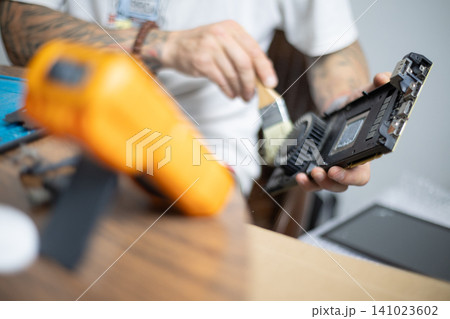 Repairing a device in a workshop using tools and techniques while seated at a wooden table during daytime Repairing a device in a workshop using tools and techniques while seated at a wooden table during daytime 141023602
