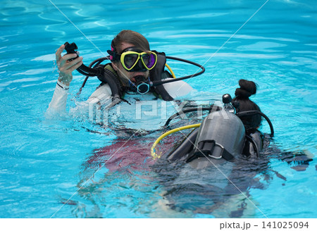 A professional diver and a novice practice diving in a pool. 141025094