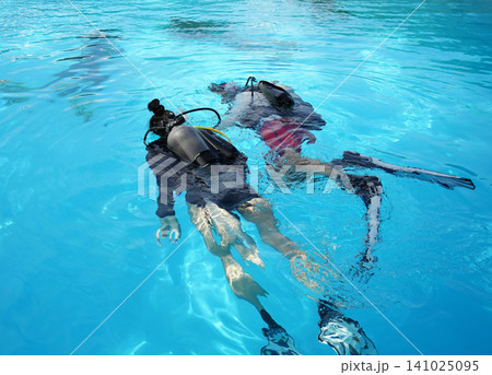 A professional diver and a novice practice diving in a pool. A professional diver and a novice practice diving in a pool. 141025095