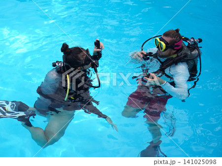 A professional diver and a novice practice diving in a pool. A professional diver and a novice practice diving in a pool. 141025098