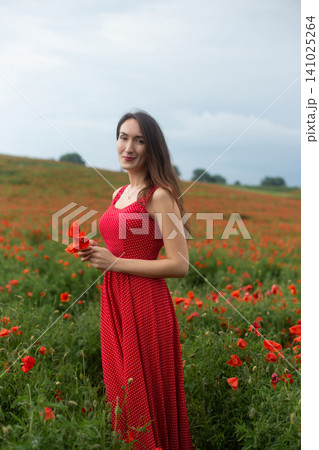 Young woman in red polka dot dress holding poppies in a field Young woman in red polka dot dress holding poppies in a field 141025264