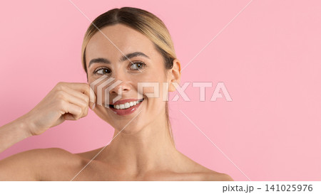 Smiling young woman pinching her cheek playfully, showcasing firm smooth skin Smiling young woman pinching her cheek playfully, showcasing firm smooth skin 141025976
