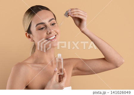 Smiling young woman applying facial serum with dropper, holding glass bottle Smiling young woman applying facial serum with dropper, holding glass bottle 141026049