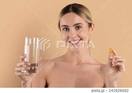 Young woman smiling while holding glass of water and softgel capsule Young woman smiling while holding glass of water and softgel capsule 141026082