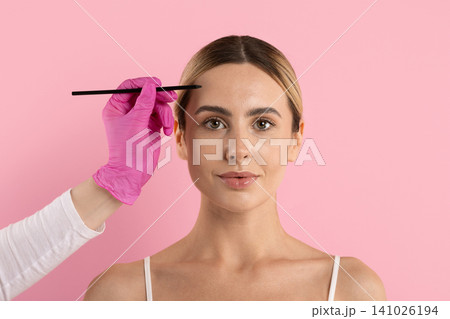 Gloved hand holding pencil beside young womans forehead, preparing to mark area 141026194