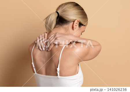 Young beautiful woman massaging her neck and upper back on beige background Young beautiful woman massaging her neck and upper back on beige background 141026236