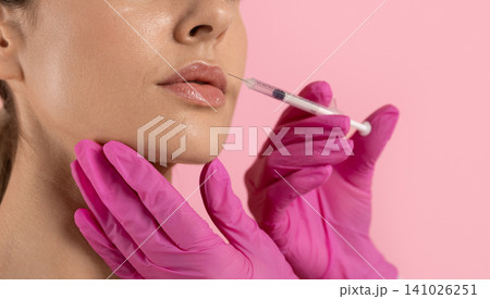 Closeup of womans lips receiving filler injection from gloved hands holding syringe 141026251