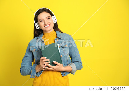 Young woman listening to audiobook on yellow background. Space for text 141026432