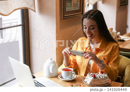 Young blogger taking picture of tea at table in cafe Young blogger taking picture of tea at table in cafe 141026449