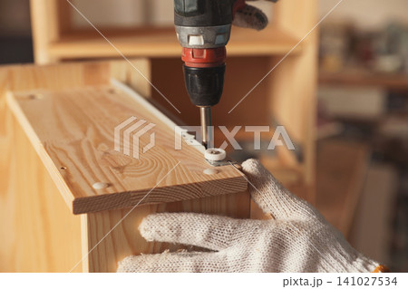 Professional carpenter twisting screw into wooden drawer in workshop, closeup 141027534