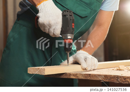 Professional carpenter twisting screw into wooden plank with drill in workshop, closeup Professional carpenter twisting screw into wooden plank with drill in workshop, closeup 141027536