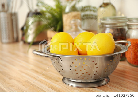 Fresh lemons in colander on wooden countertop. Kitchen interior element Fresh lemons in colander on wooden countertop. Kitchen interior element 141027550