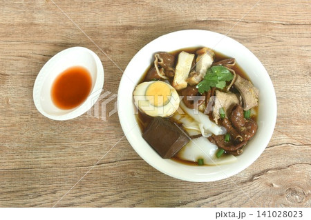 Chinese rice flour paste with pork and entrails topping boiled egg in herb brown soup on bowl dressing spicy chili vinegar sauce Chinese rice flour paste with pork and entrails topping boiled egg in herb brown soup on bowl dressing spicy chili vinegar sauce 141028023