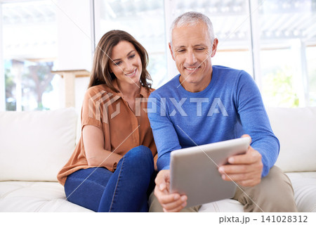 Couple, tablet and happy on sofa to relax with reading, search or app for bonding in home living room. People, woman and mature man on digital touchscreen on lounge couch with web streaming in house Couple, tablet and happy on sofa to relax with reading, search or app for bonding in home living room. People, woman and mature man on digital touchscreen on lounge couch with web streaming in house 141028312