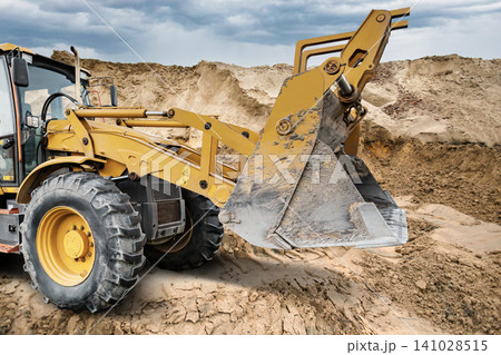 The universal excavator loader works at a construction site moving dirt and materials. Dust rises around the equipment during a busy afternoon 141028515