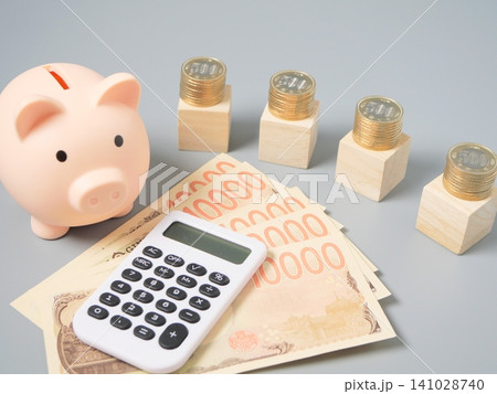 積み上げた硬貨と電卓、お札、木製ブロックを使った資産形成・家計管理・投資イメージ（グレー背景・コピー 141028740
