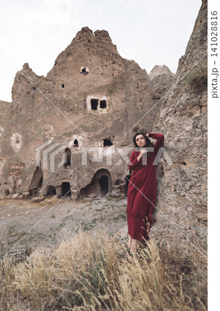 a beautiful girl sits and enjoys the view of the ancient architecture of the caves in Cappadocia. a beautiful girl sits and enjoys the view of the ancient architecture of the caves in Cappadocia. 141028816