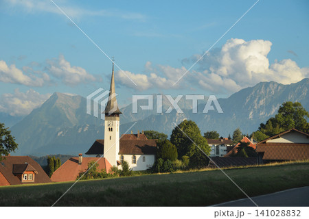 Picturesque alpine village with a church spire against a mountain backdrop Picturesque alpine village with a church spire against a mountain backdrop 141028832