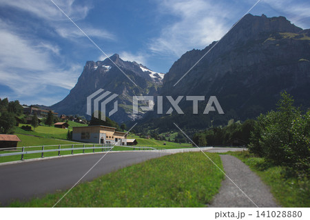 Scenic asphalt road leading towards massive Alpine mountains in a green valley Scenic asphalt road leading towards massive Alpine mountains in a green valley 141028880