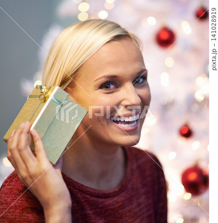 Christmas, gift and excited woman listening with holiday surprise, celebration and tradition at night. Portrait of a young person by tree and bokeh lights with present, box and thanksgiving at home Christmas, gift and excited woman listening with holiday surprise, celebration and tradition at night. Portrait of a young person by tree and bokeh lights with present, box and thanksgiving at home 141028919