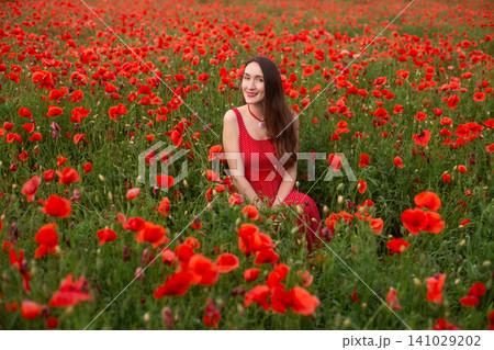 Woman in red polka dot dress sitting in a vast poppy field Woman in red polka dot dress sitting in a vast poppy field 141029202