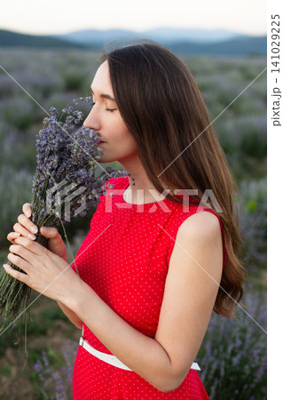 Young woman in red polka dot dress smelling lavender bouquet in a field Young woman in red polka dot dress smelling lavender bouquet in a field 141029225
