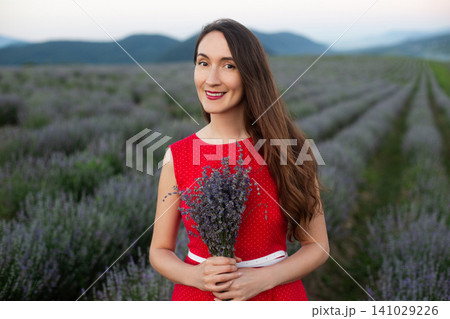 Smiling young woman in red polka dot dress holding lavender bouquet in a field Smiling young woman in red polka dot dress holding lavender bouquet in a field 141029226