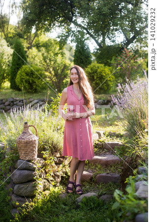 Smiling young woman in pink polka dot dress holding wine glass in a summer garden 141029232