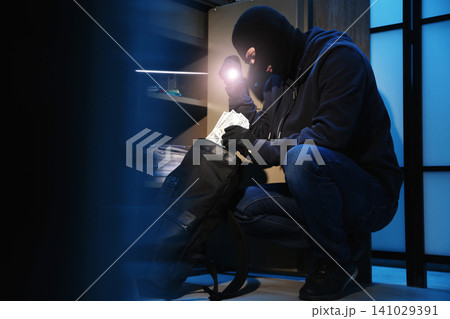 Thief taking money out of steel safe indoors at night Thief taking money out of steel safe indoors at night 141029391