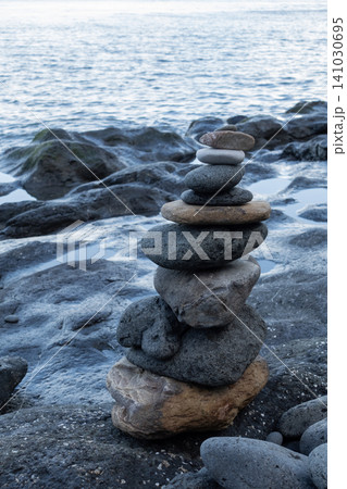 A vertical composition of a balanced stone stack on a rocky beach against a sea background A vertical composition of a balanced stone stack on a rocky beach against a sea background 141030695