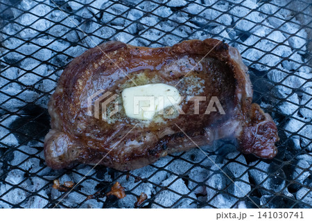 Close-up of a juicy beef steak grilling on a wire rack over hot charcoal with a piece of butter melting on top Close-up of a juicy beef steak grilling on a wire rack over hot charcoal with a piece of butter melting on top 141030741
