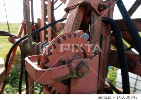 Close-up of a rusty metal gear mechanism on agricultural machinery with a blurred farm field in the background Close-up of a rusty metal gear mechanism on agricultural machinery with a blurred farm field in the background 141030745