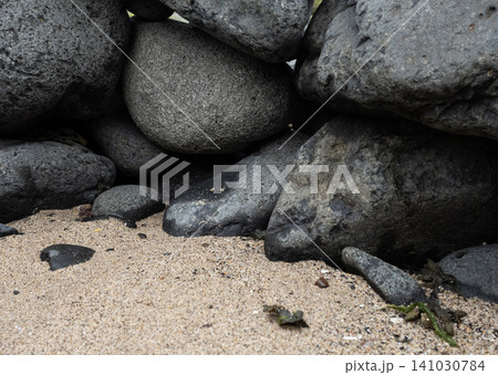 Close-up of stacked large dark grey volcanic rocks and boulders on a sandy beach Close-up of stacked large dark grey volcanic rocks and boulders on a sandy beach 141030784