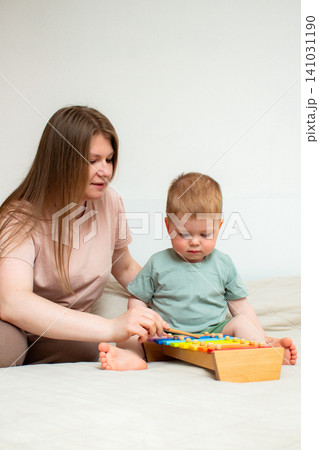 Little boy exploring sounds by hitting xylophone keys. Each note teaches pitch differentiation. Fine motor growth through gripping mallet. Parent help in child education Little boy exploring sounds by hitting xylophone keys. Each note teaches pitch differentiation. Fine motor growth through gripping mallet. Parent help in child education 141031190